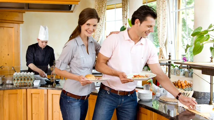 Coppia si serve al buffet della colazione in hotel con cuoco che cucina uova sullo sfondo